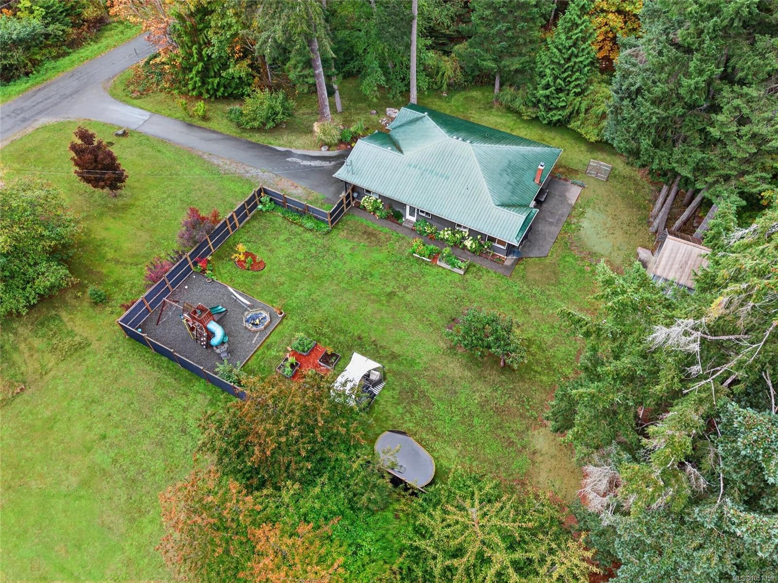 Aerial view of a green-roofed house with a fenced playground and spacious, tree-lined lawn.