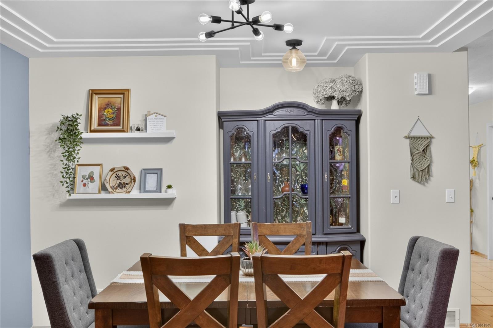 Furnished dining room with a wooden table, dark glass-front cabinet, and layered tray ceiling.