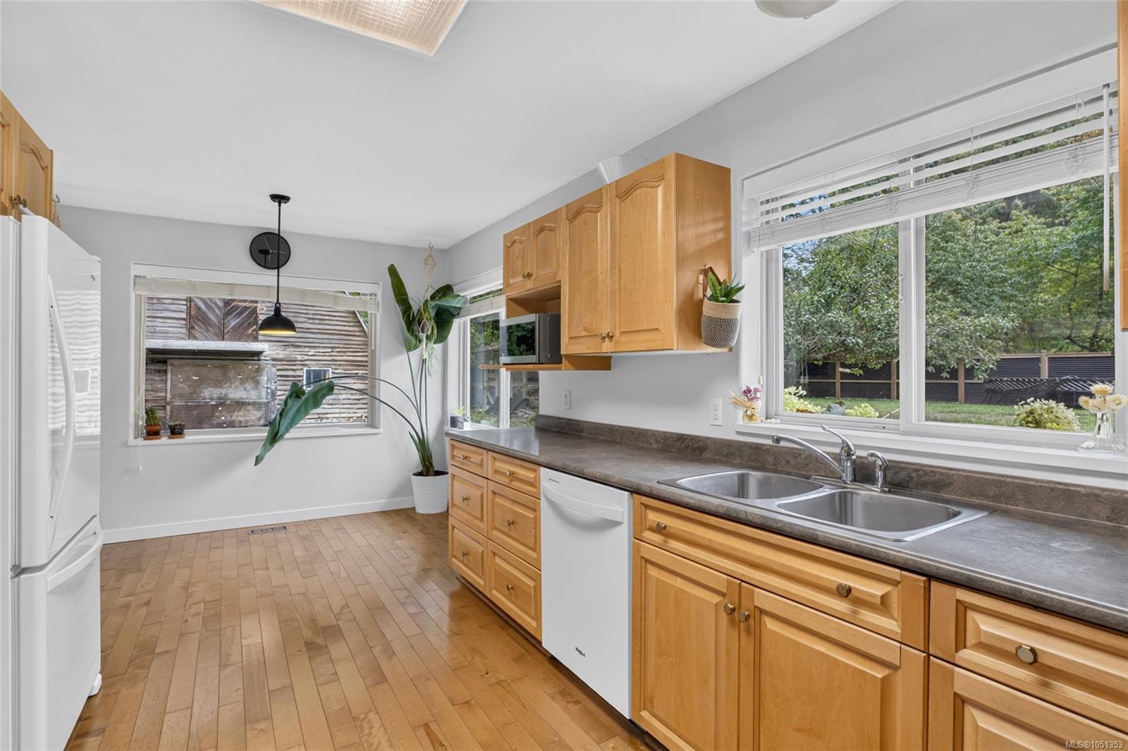 Kitchen with honey-colored cabinets, a double sink, and large windows overlooking greenery.