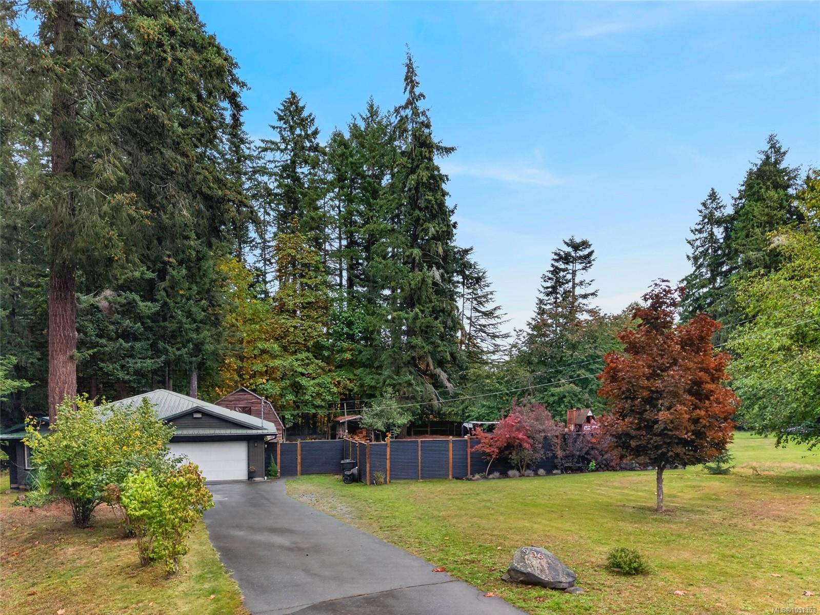 Home partly screened by mature trees, with a paved driveway, garage, fenced yard, and 936 marker.