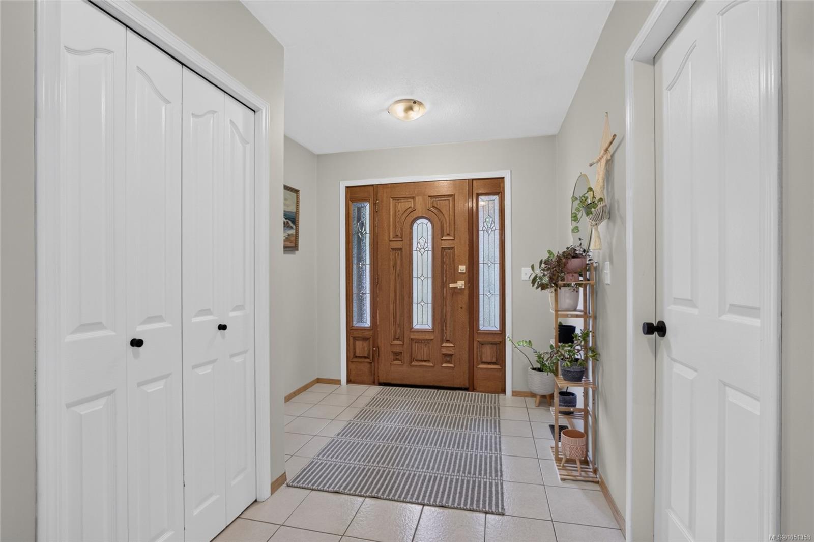 Entry foyer with a decorative-glass wood front door, tiled floor, white closets, and a striped runner.