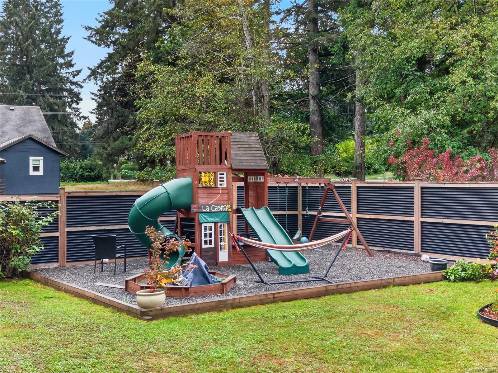 Backyard play area with a wooden playset, green slides, swings, and hammock.