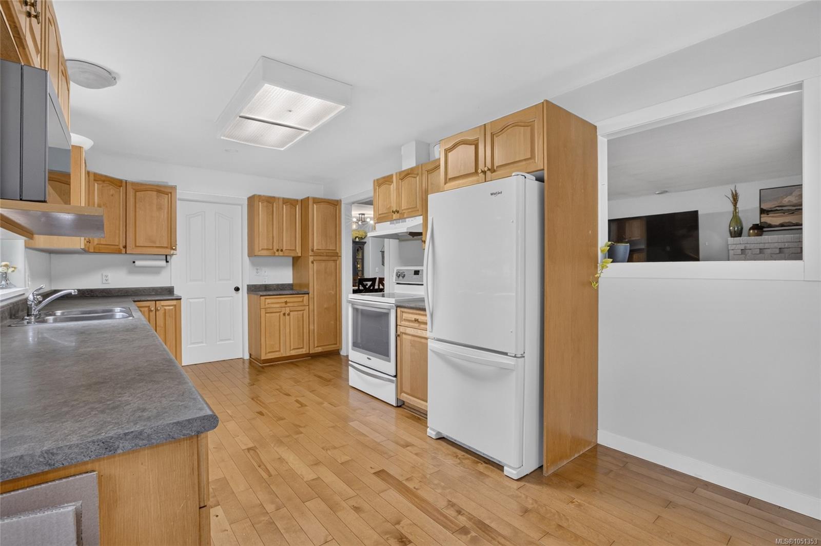 Kitchen with honey-colored wood cabinets, gray countertops, white appliances, and hardwood floors.
