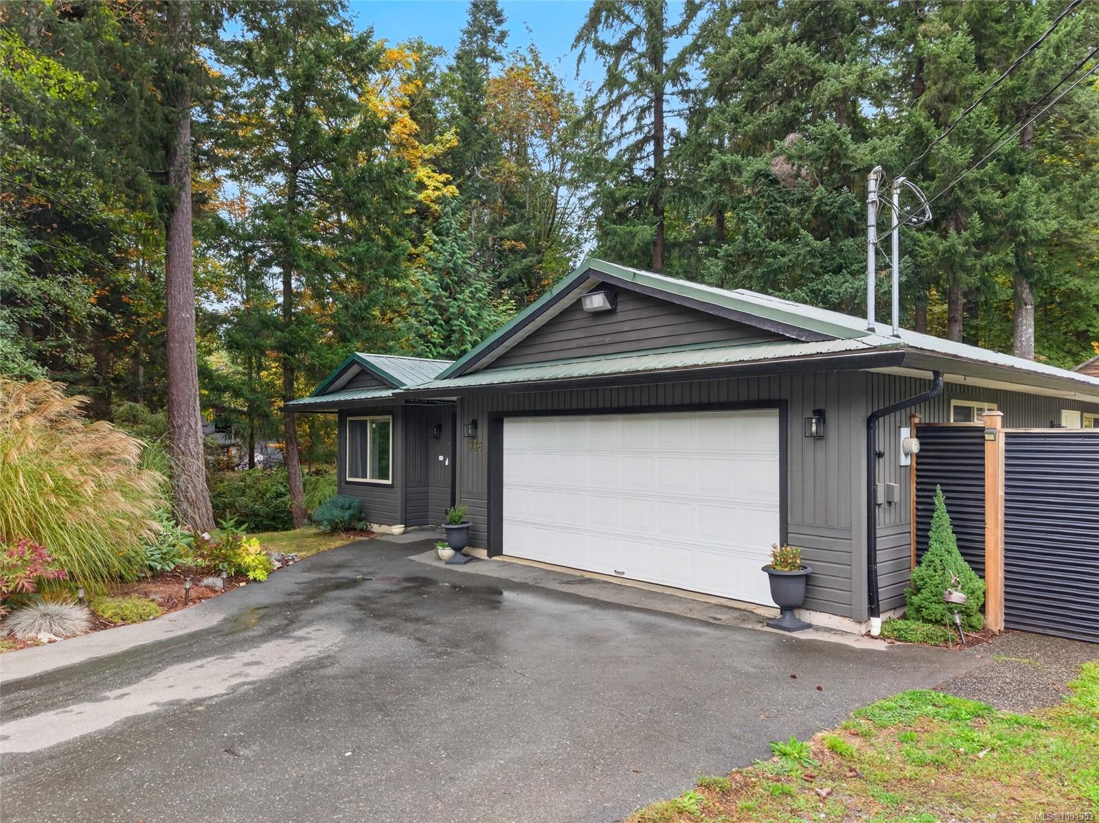 Dark gray home with a wide white garage door, green metal roof, and wooded surroundings.