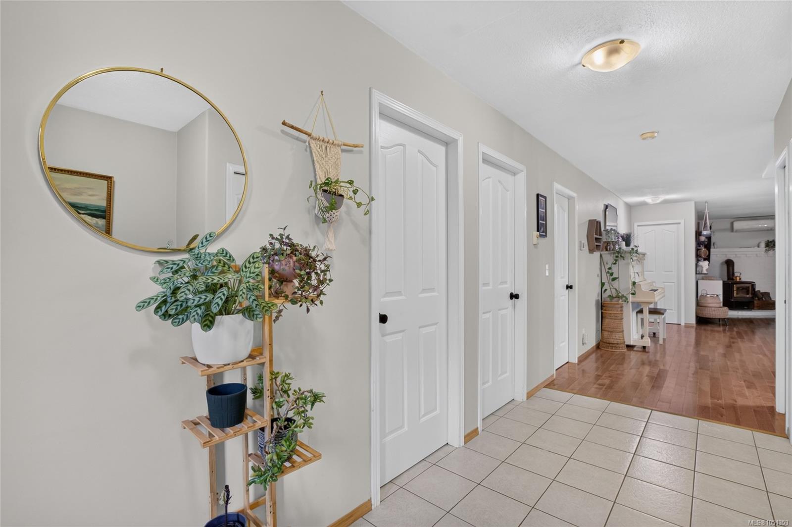Hallway with white paneled doors, tiled entry, gold-framed mirror, and potted plants.