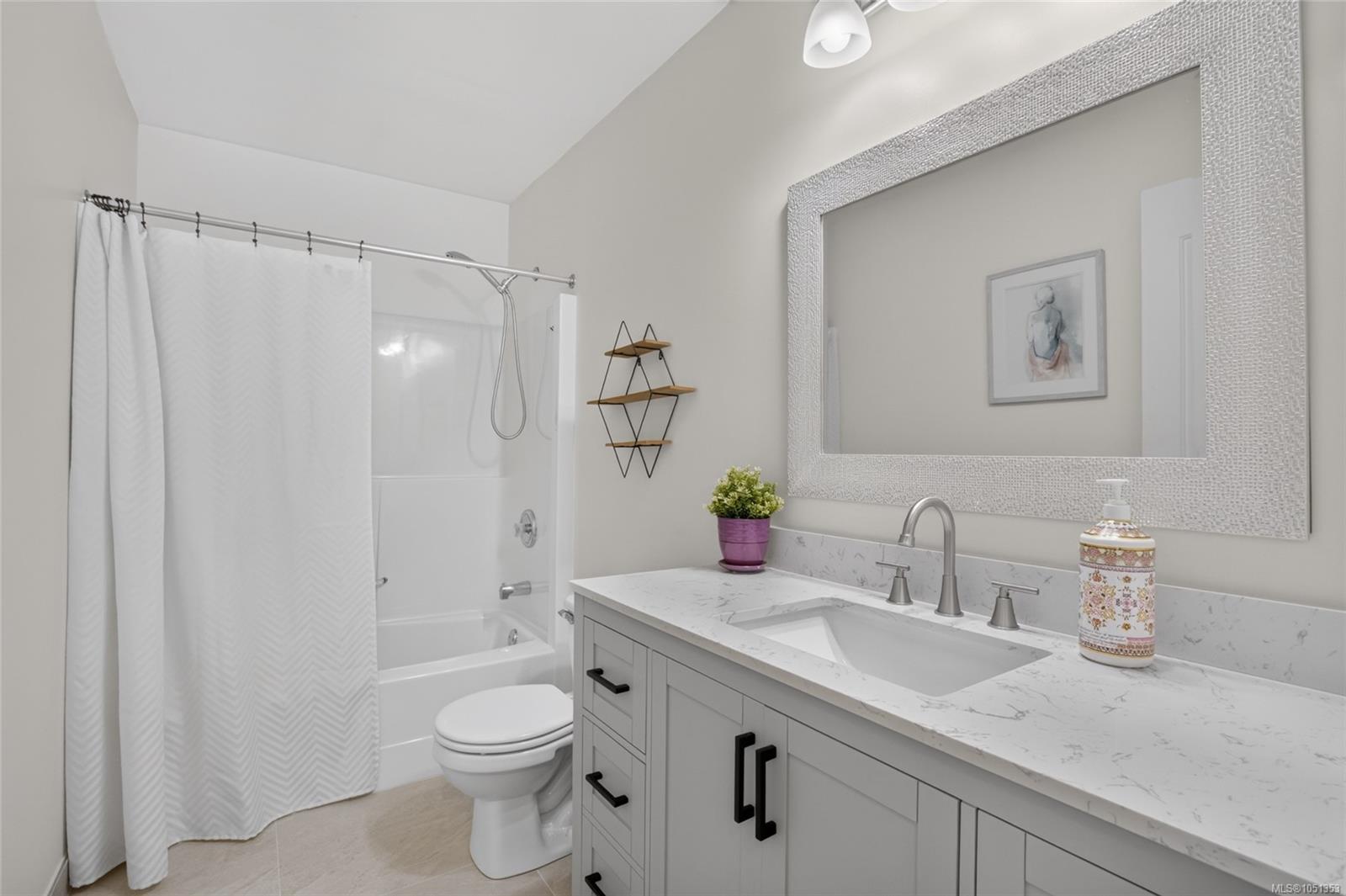 Bathroom with a gray vanity, marble-look counter, framed mirror, and white tub behind a patterned curtain.