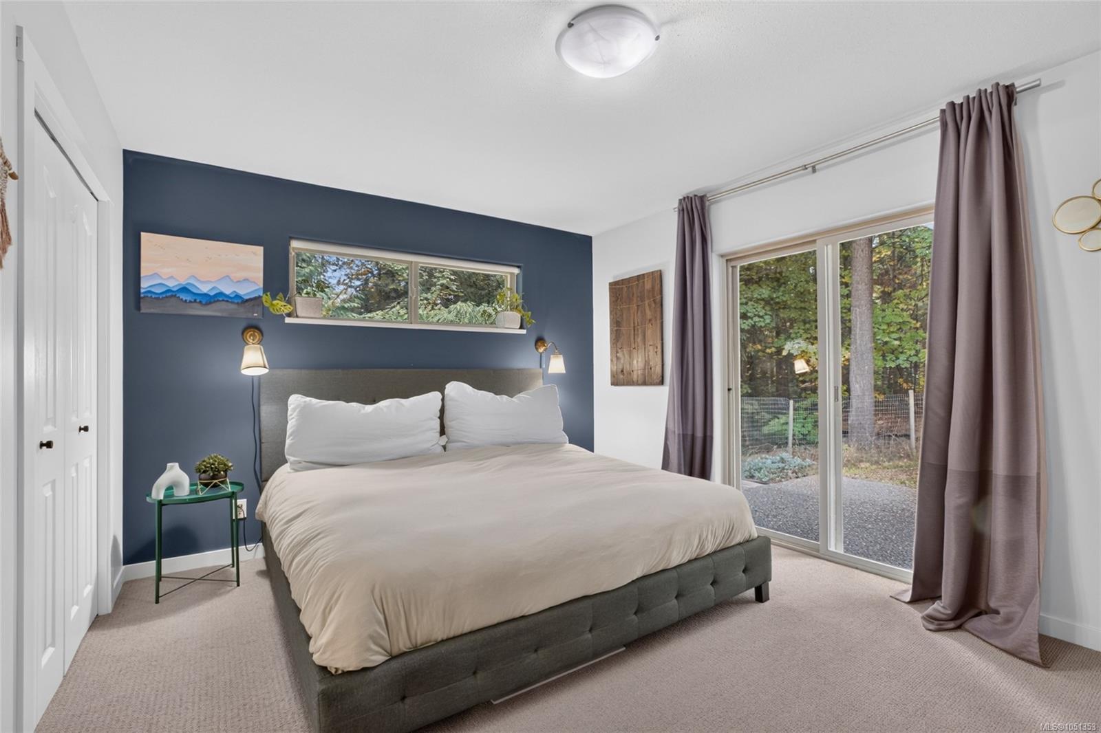 Bedroom with a navy accent wall, large bed, and sliding glass doors overlooking trees.