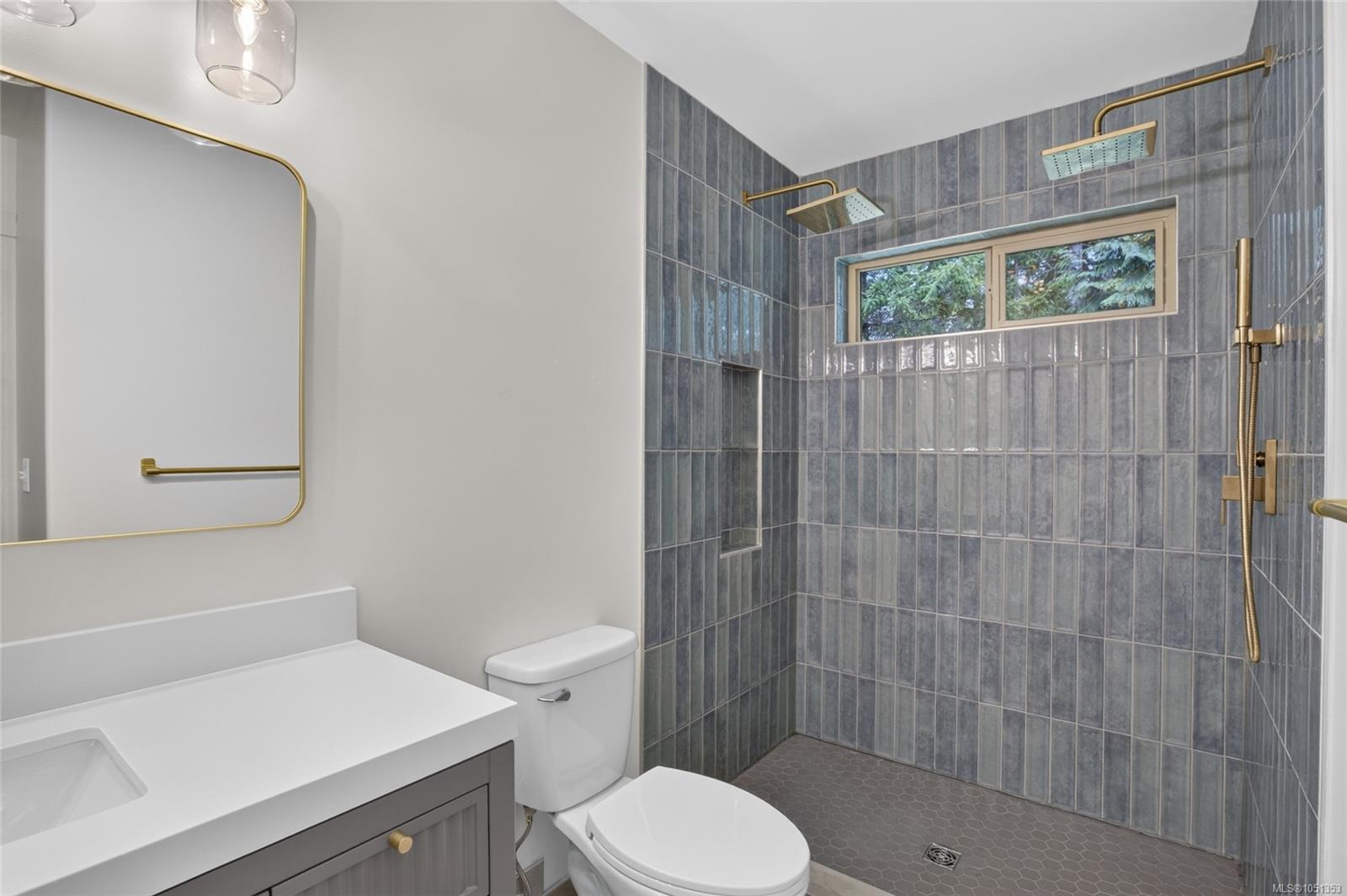 Bathroom with a gray-tiled walk-in shower, two brass showerheads, and a high window.