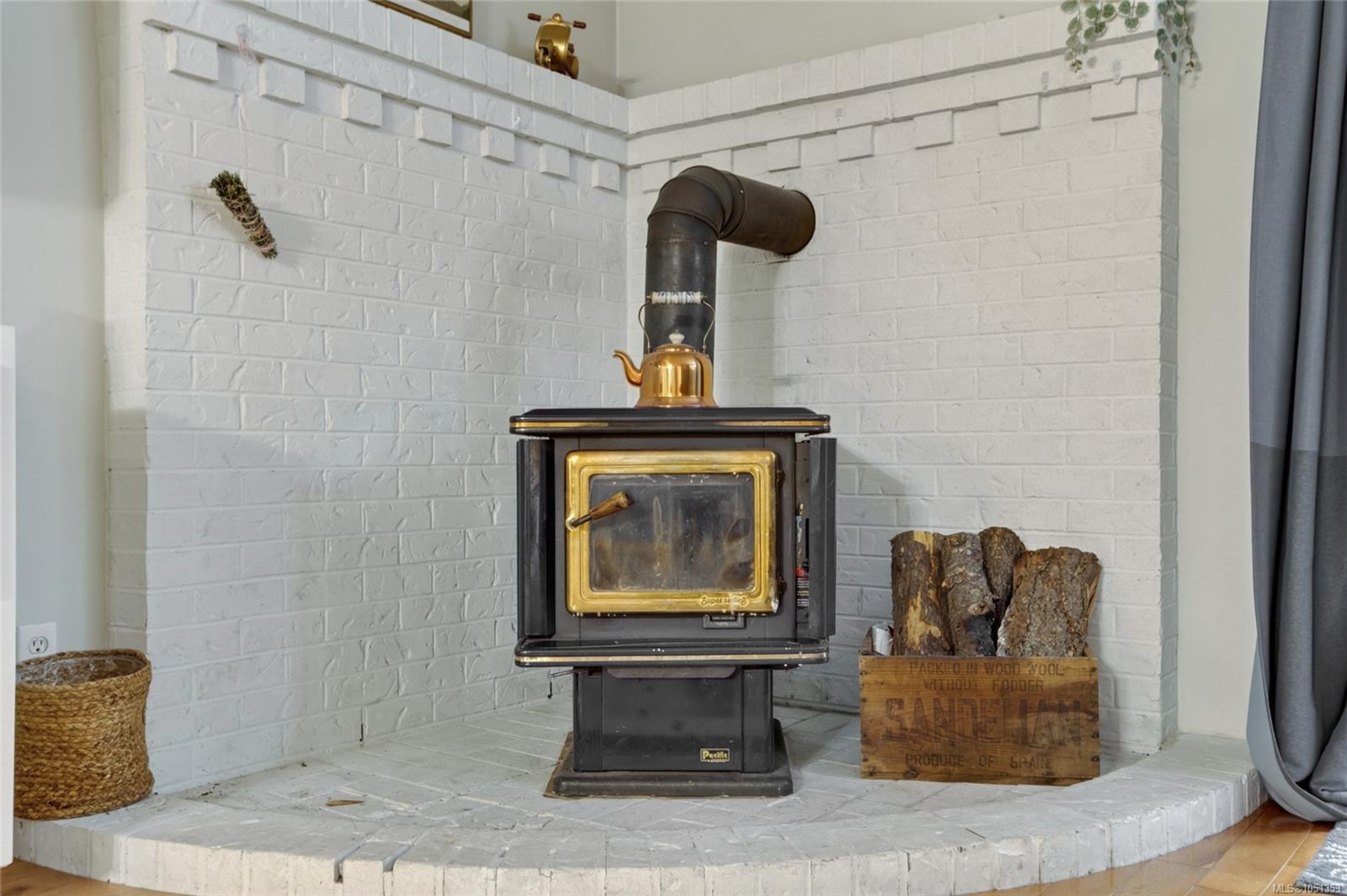 Wood-burning stove with brass trim and a copper kettle on a white brick hearth.