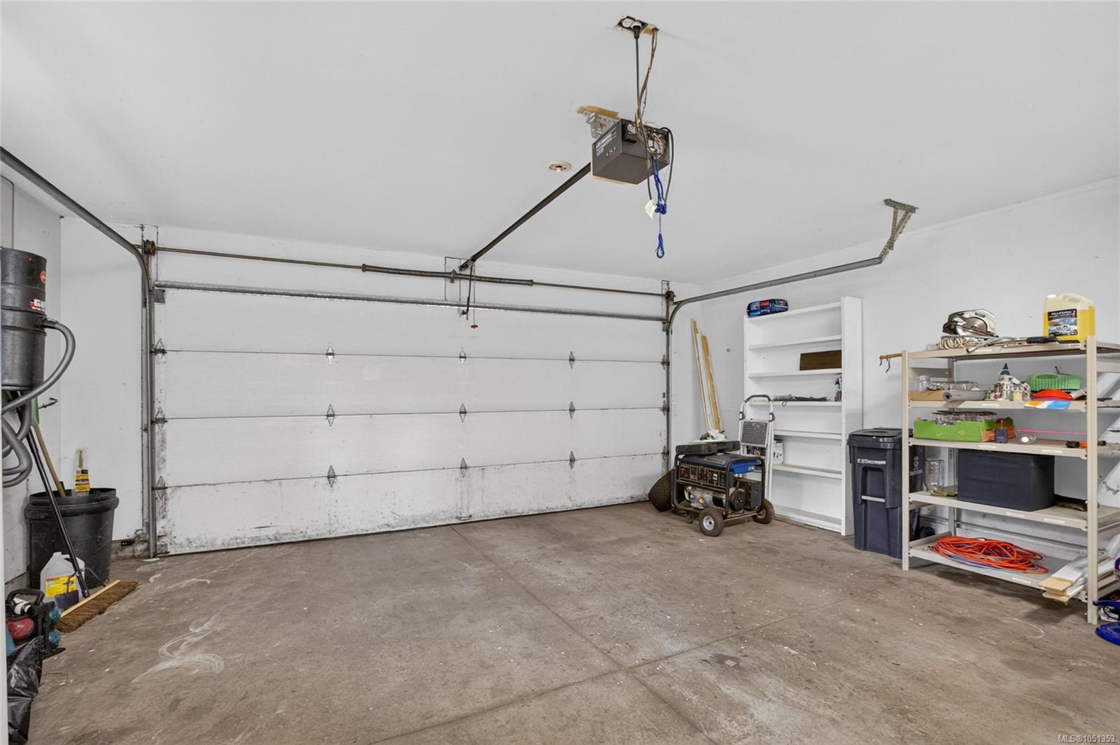 Garage with a wide overhead door, concrete floor, storage shelves, and portable generator.