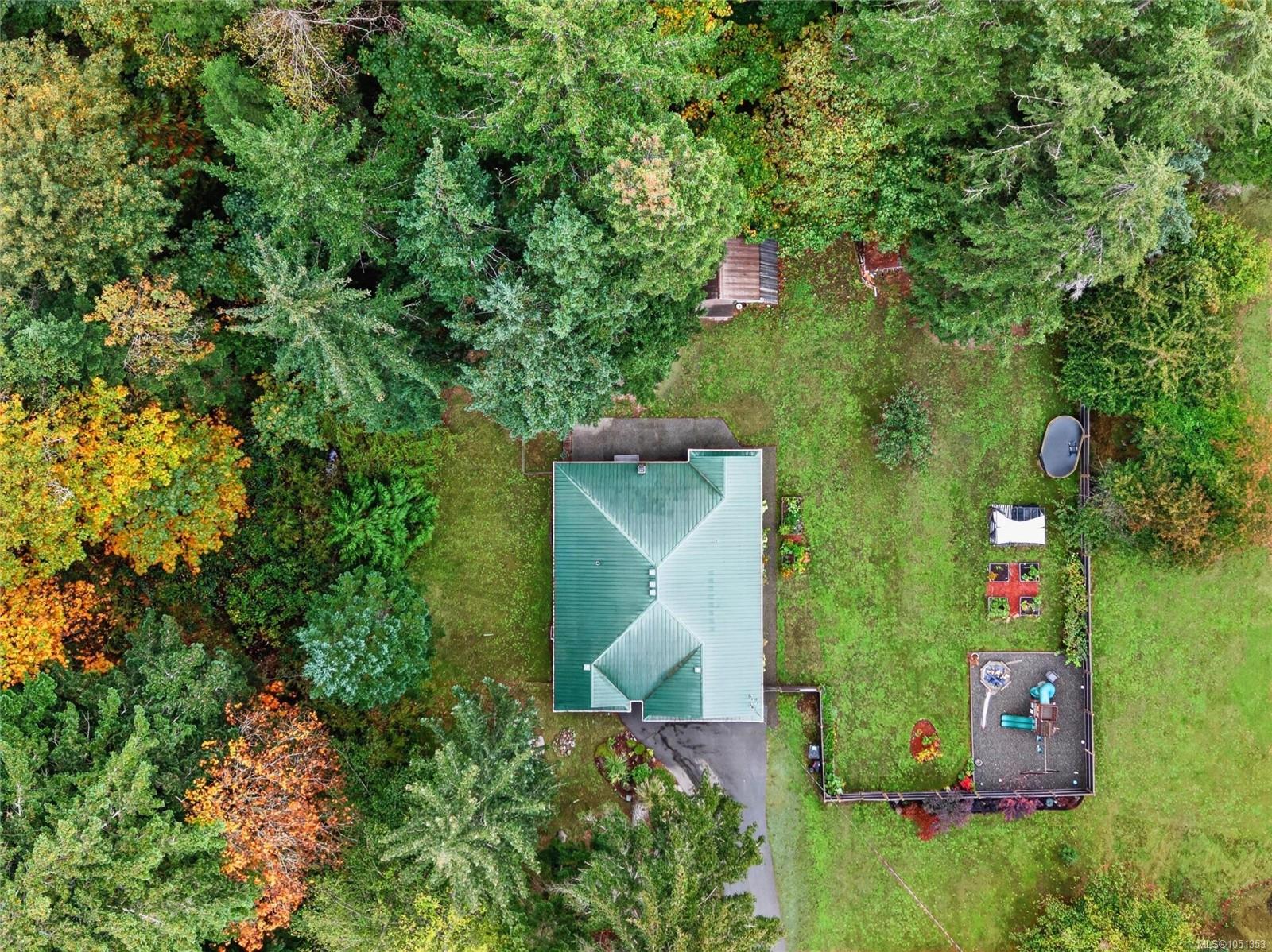 Aerial view of a green-roofed home on a wooded lot with a lawn and deck.