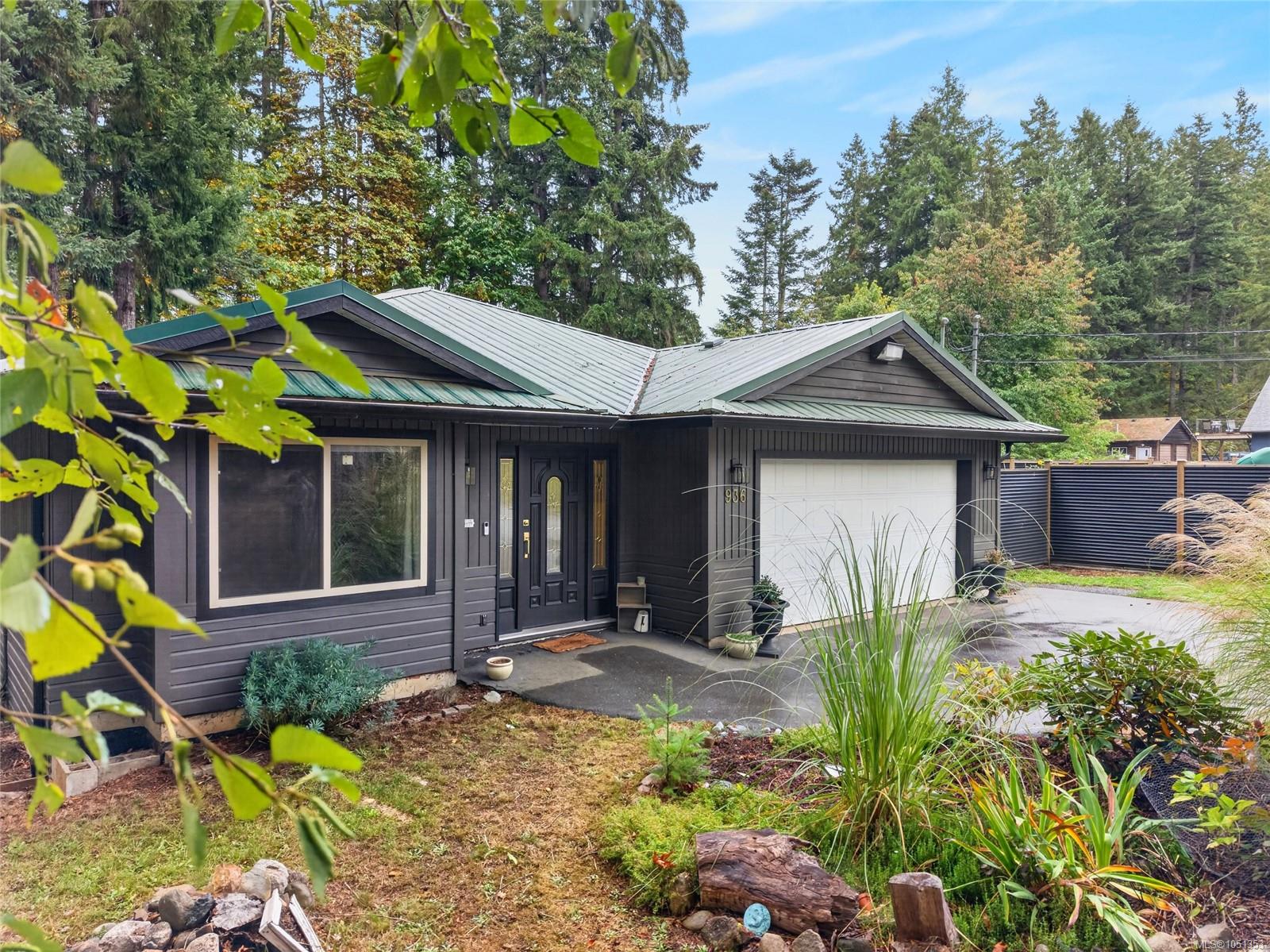 Dark-sided home with a green metal roof, attached garage, and landscaped front yard.