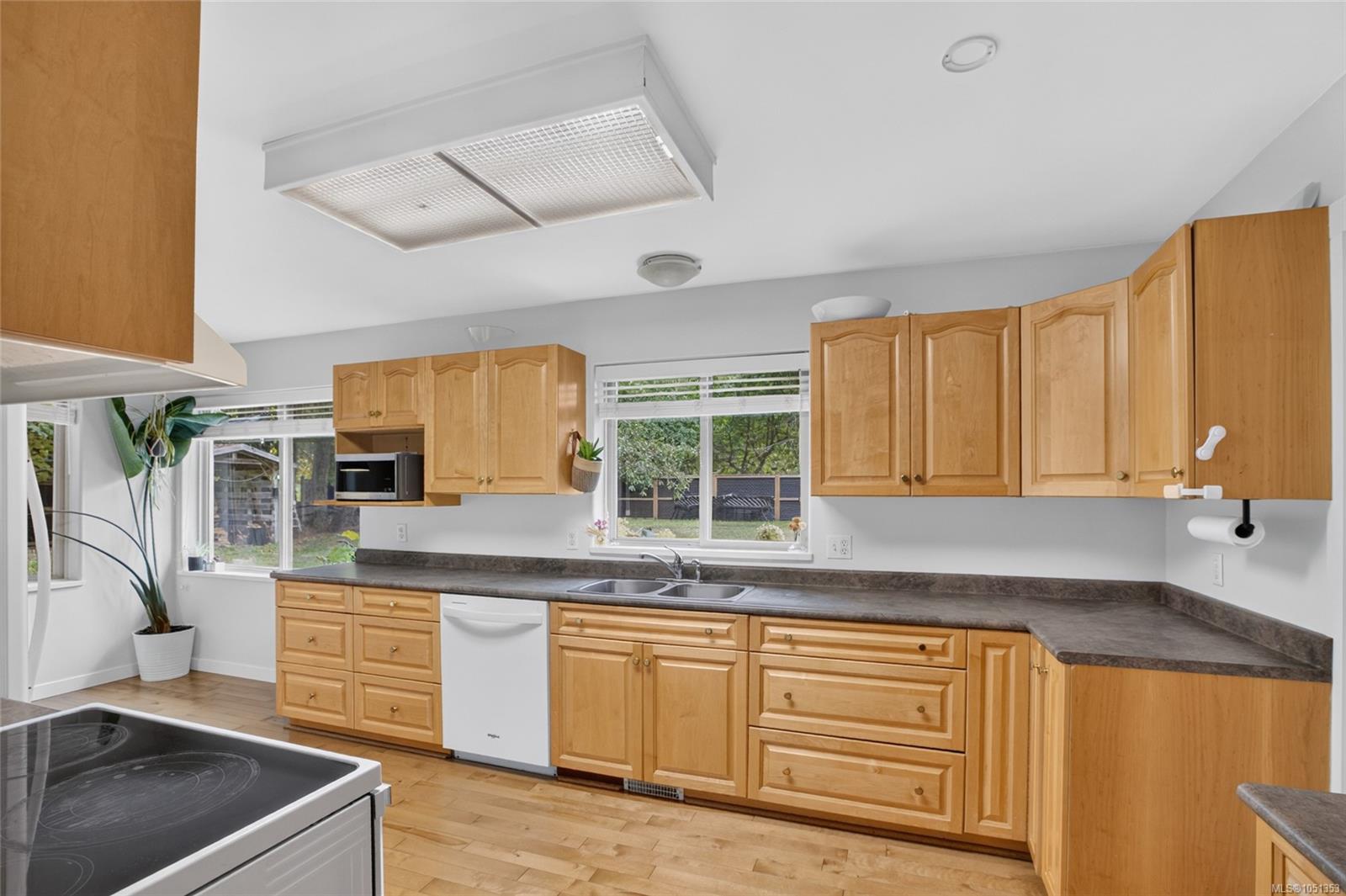 Kitchen with honey-colored wood cabinets, dark countertops, and windows overlooking the yard.