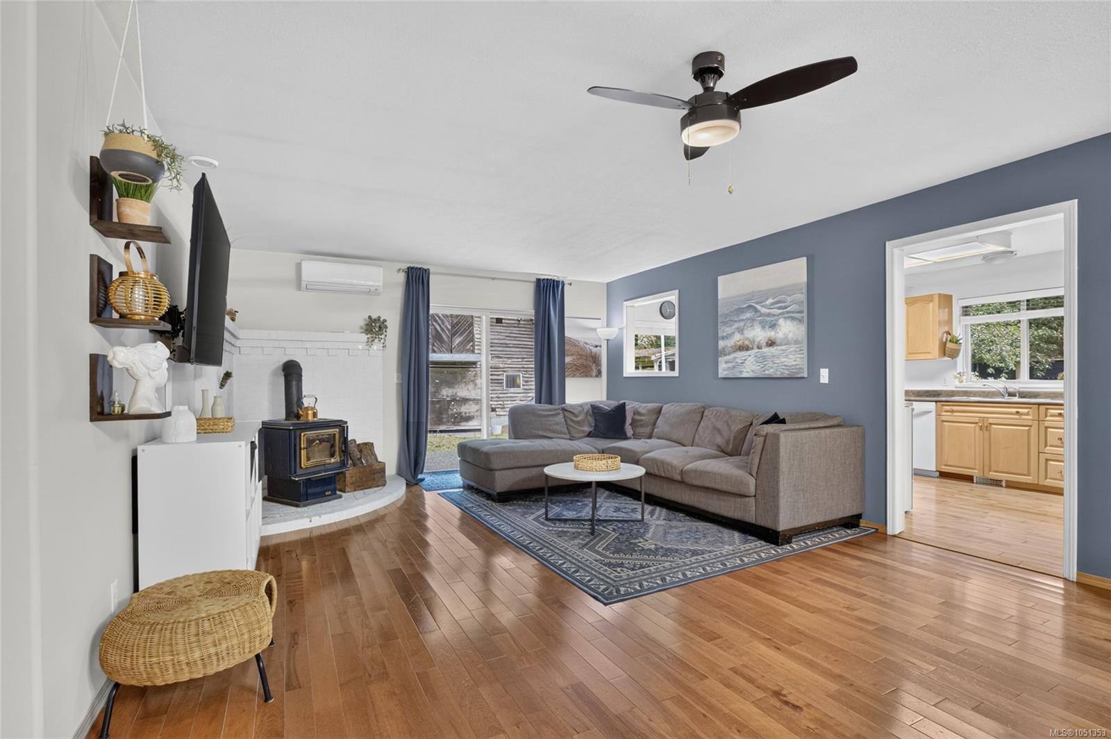 Living room with a gray sectional, hardwood floors, and a black wood-burning stove.