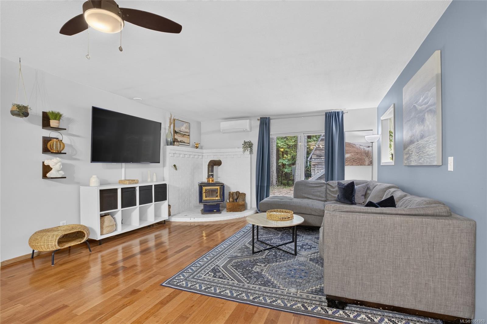 Living room with a gray sectional, patterned rug, hardwood floors, and blue wood stove.