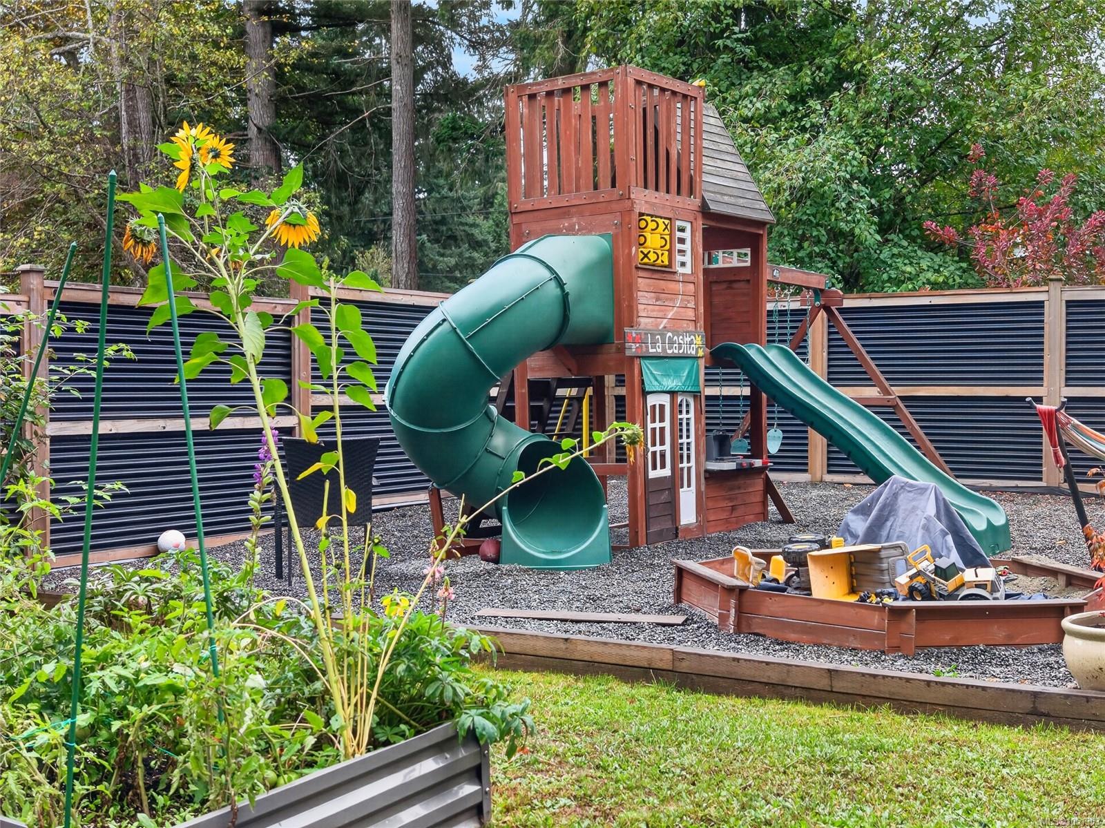 Backyard playground with a wooden play structure, green tube slide, swings, and sandbox.