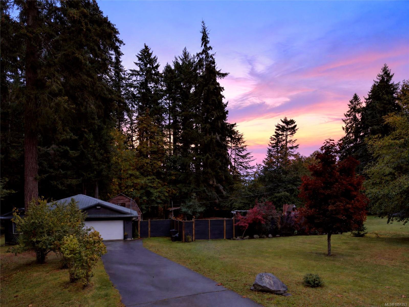 Home and garage at the end of a paved driveway, framed by mature trees beneath a colorful dusk sky.