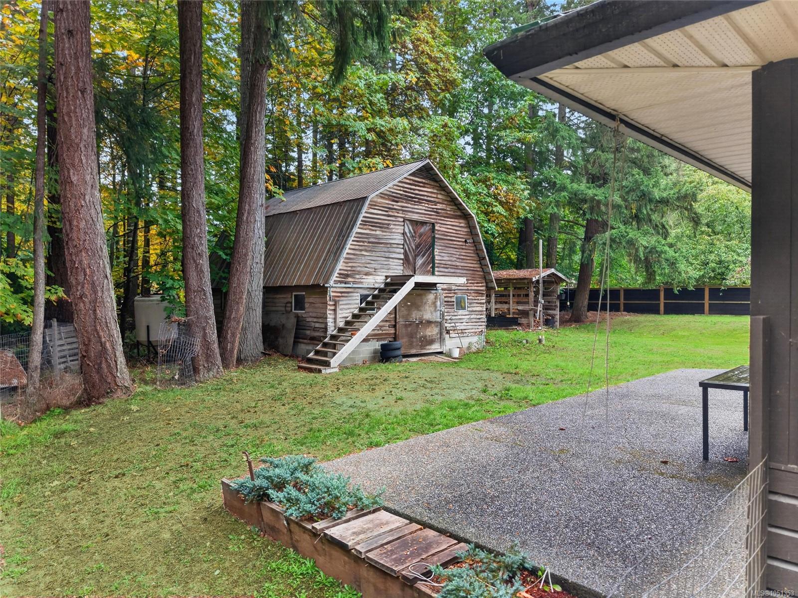 Weathered wooden barn with exterior stairs in a tree-lined yard beside a gravel driveway.