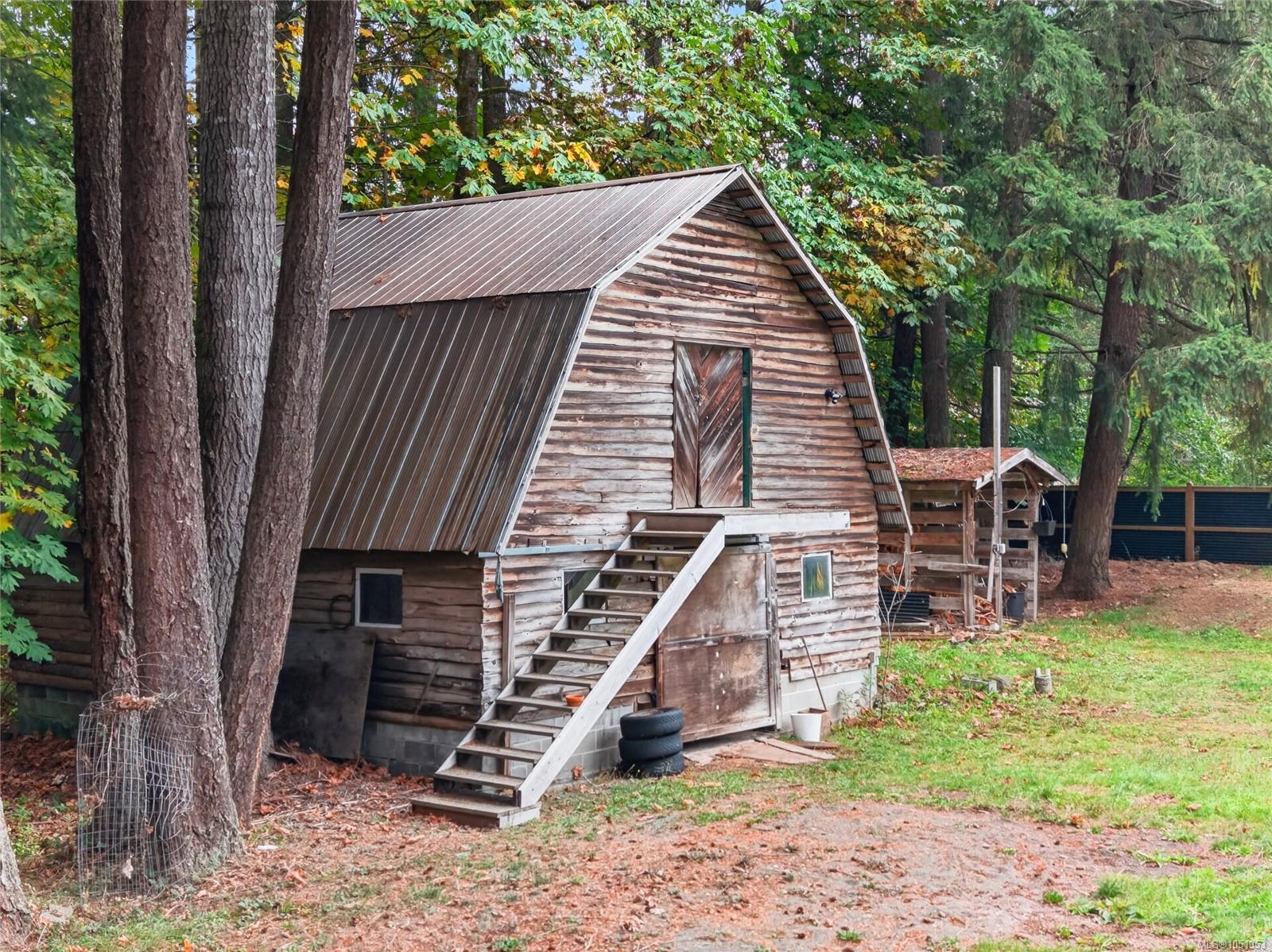 Weathered wooden outbuilding with exterior stairs among tall trees.