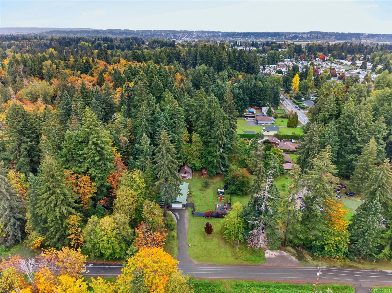 Aerial view of a wooded Courtenay property with a home, driveway, and autumn trees.