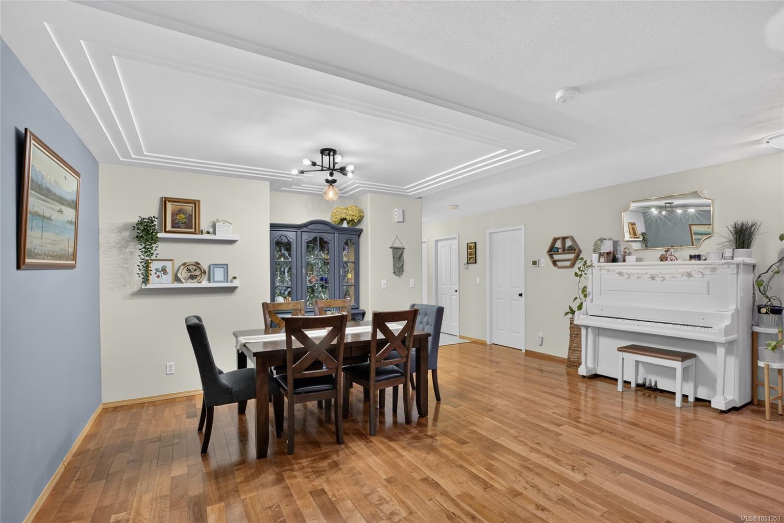 Dining room with a dark wood table, white piano, hardwood floors, and a layered tray ceiling.