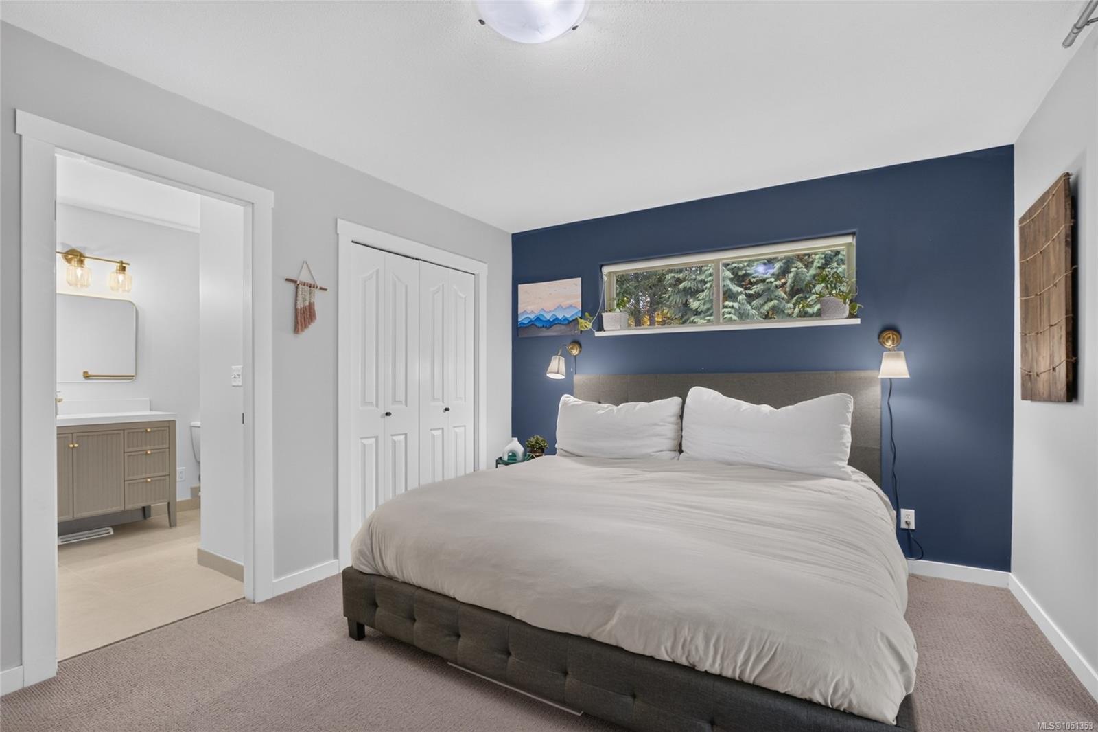 Bedroom with a large bed, navy accent wall, and narrow window overlooking trees.