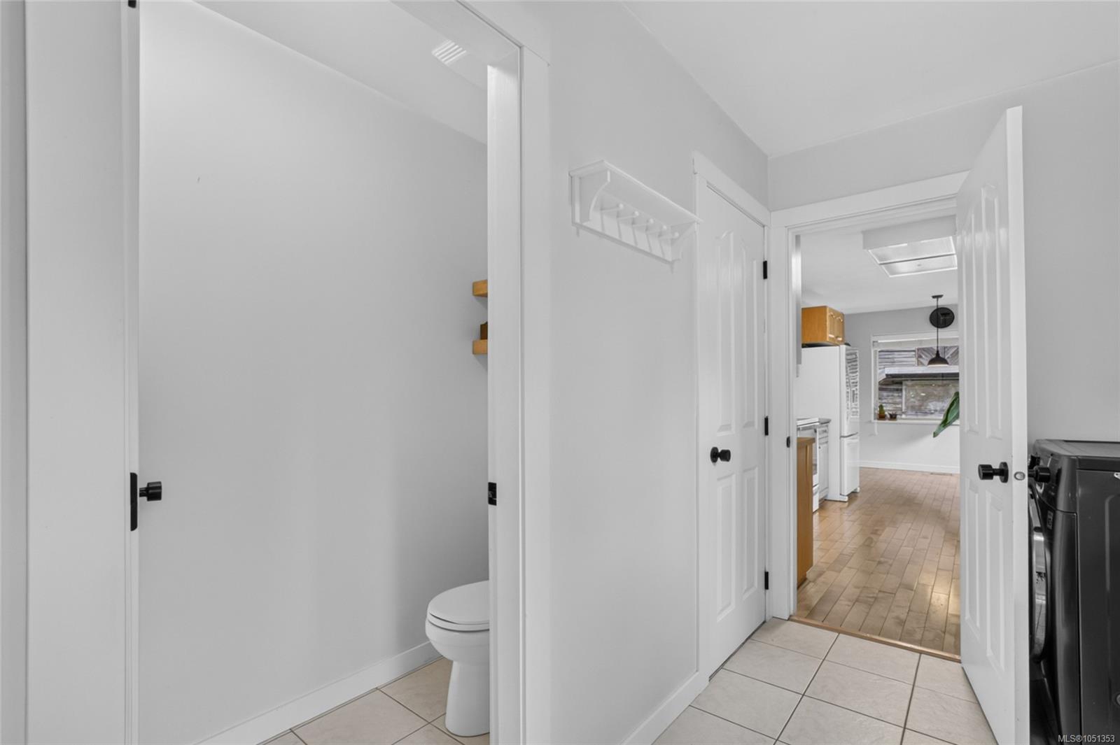 Tiled hallway opens to a toilet room, with the kitchen and laundry appliances visible beyond.