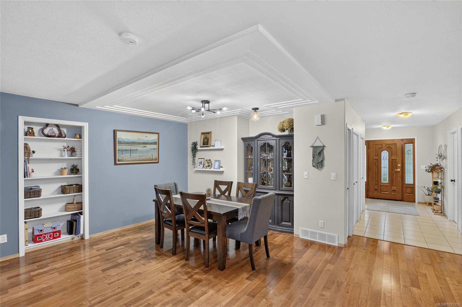 Dining room with a dark wood table, blue accent wall, built-in shelves, and a view into the tiled entry hall.