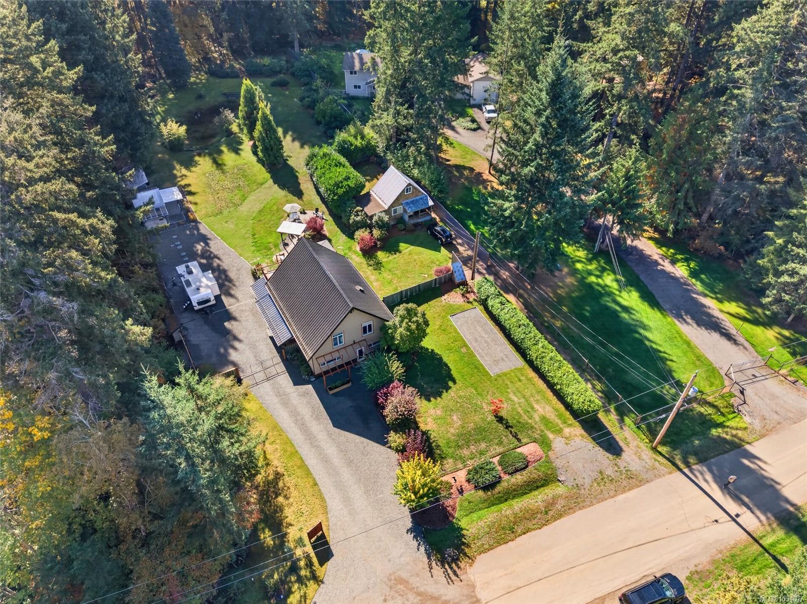 Aerial view of a wooded property with two homes, landscaped lawns, and a long driveway.