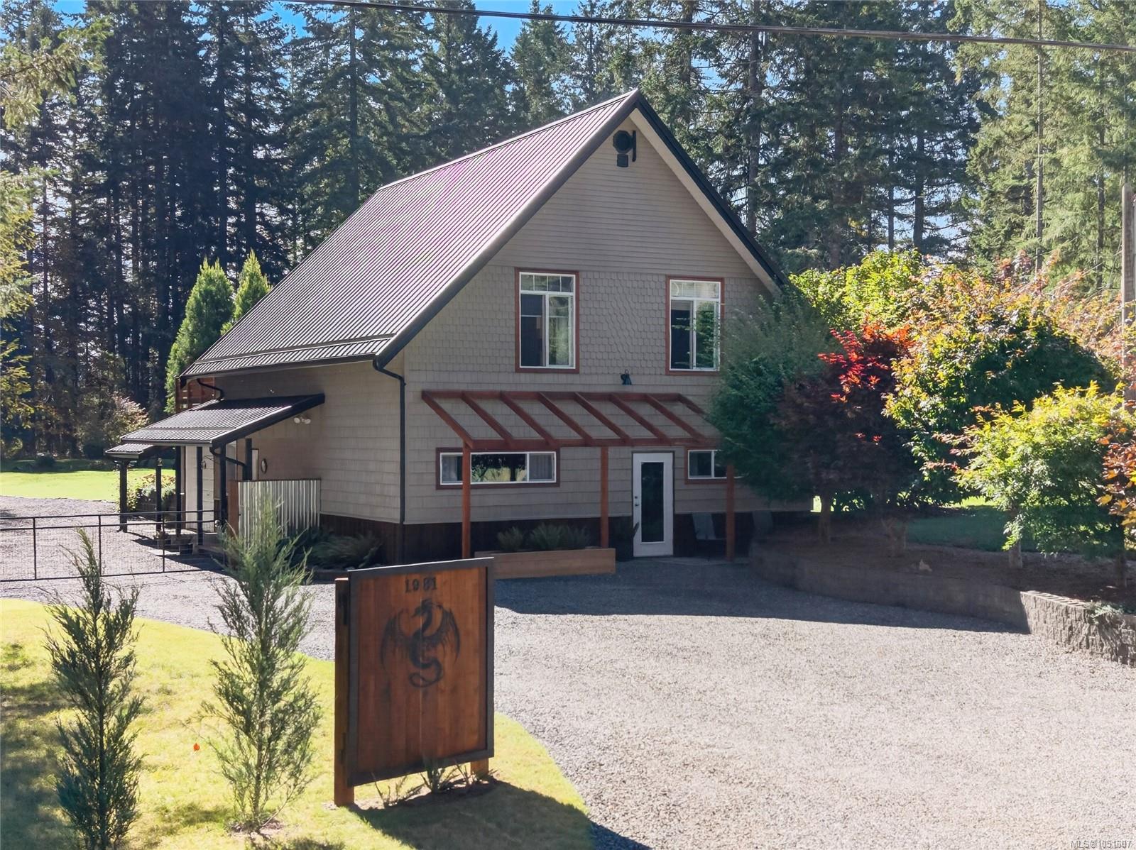 Two-story home with a steep metal gable roof, gravel driveway, and wooded surroundings.
