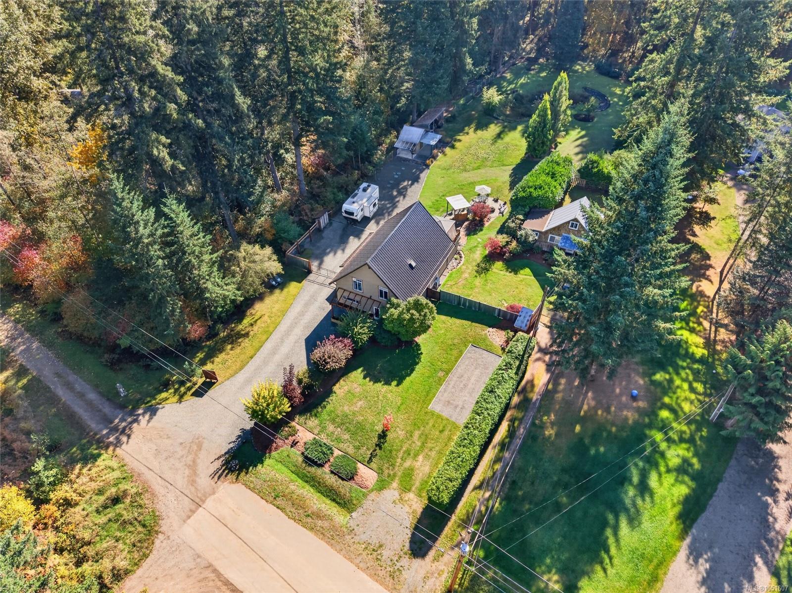 Aerial view of a detached home surrounded by trees, with a broad lawn and long driveway.