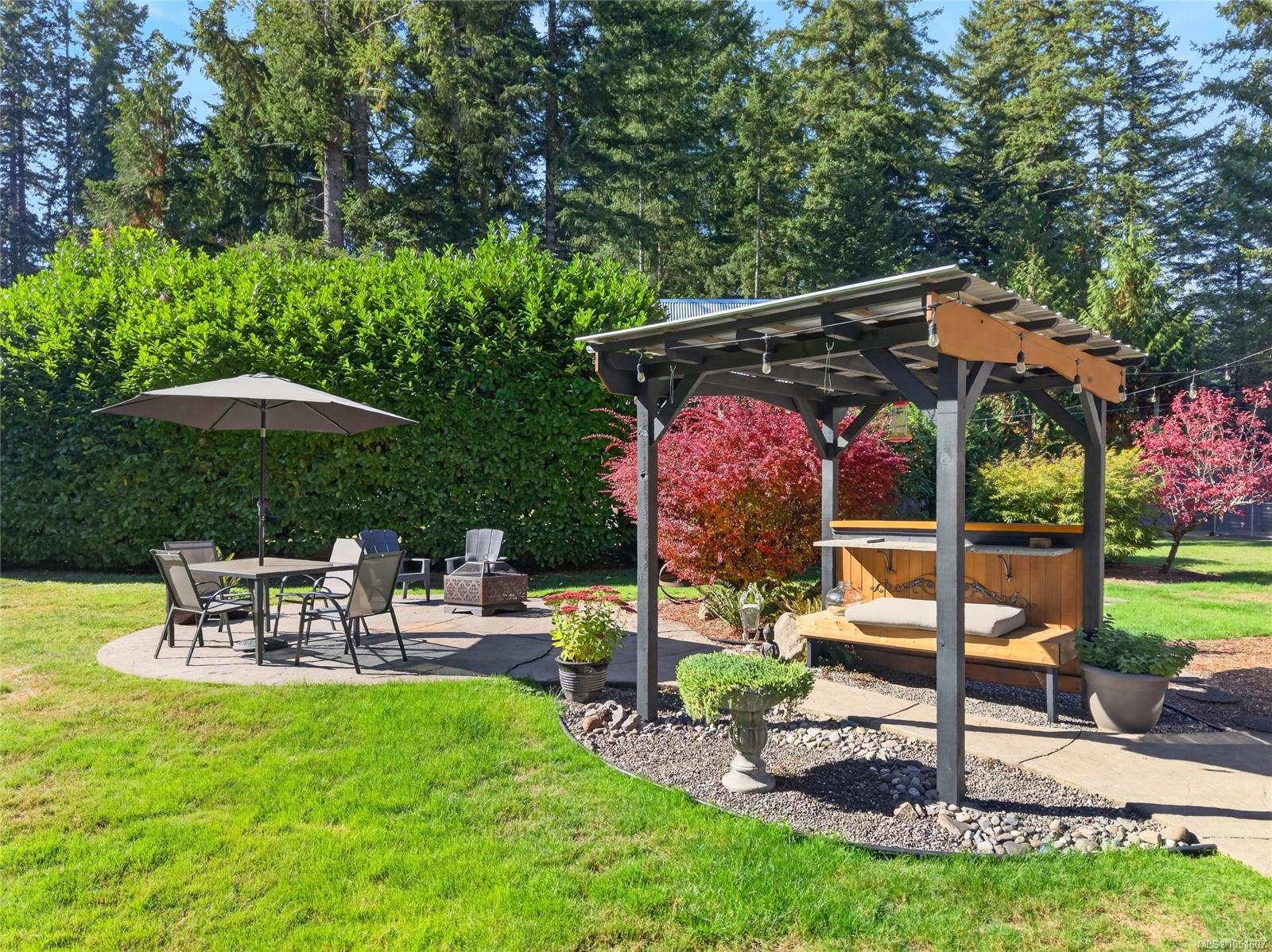 Backyard patio with a covered pergola bar, cushioned bench, and umbrella-shaded dining table.