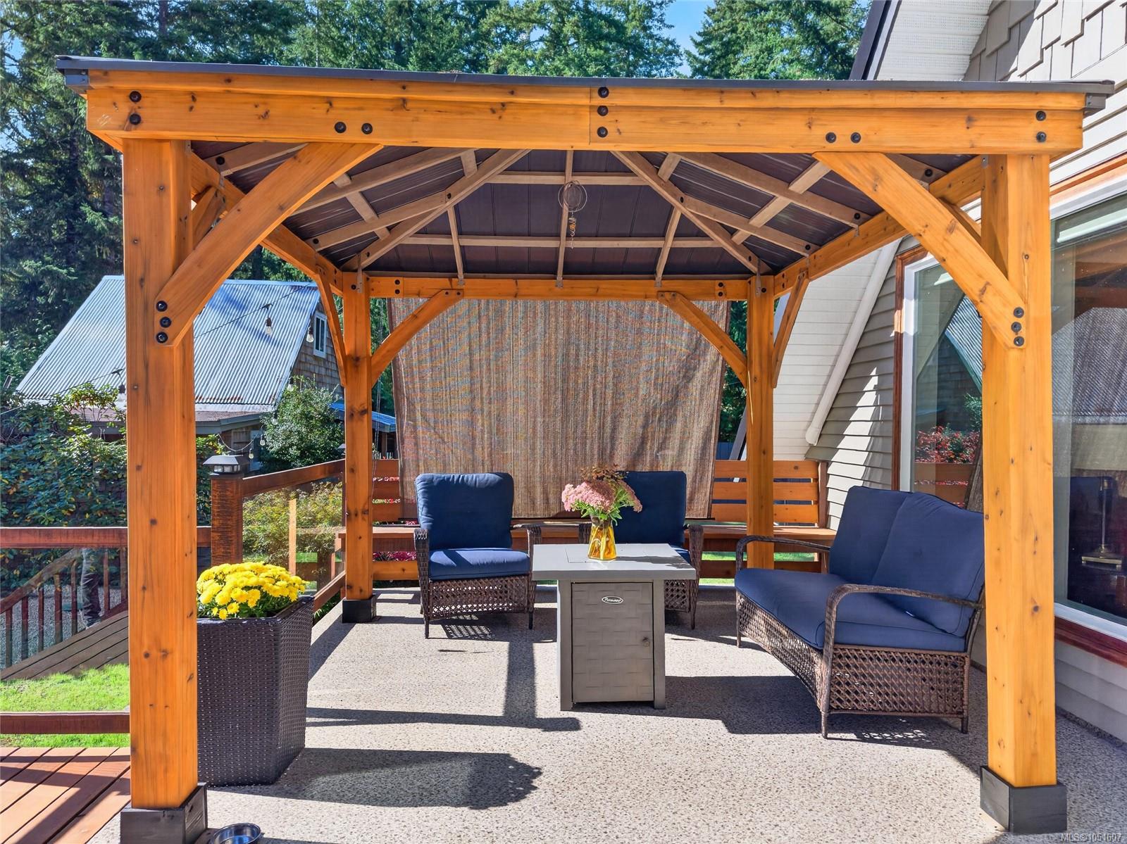 Outdoor patio under a timber pergola, with blue-cushioned seating and flower planters.