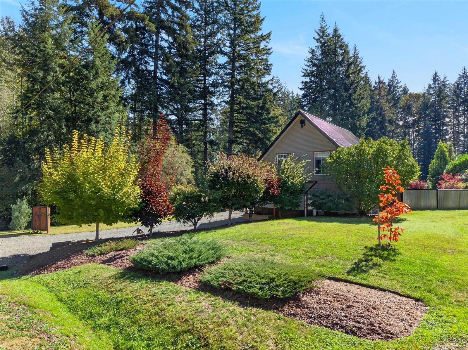 Gabled house among evergreens, with a landscaped lawn, colorful trees, and a gravel driveway.