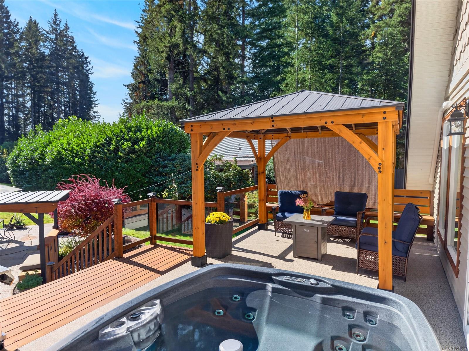Patio with a hot tub, covered pergola, and outdoor seating surrounded by trees.