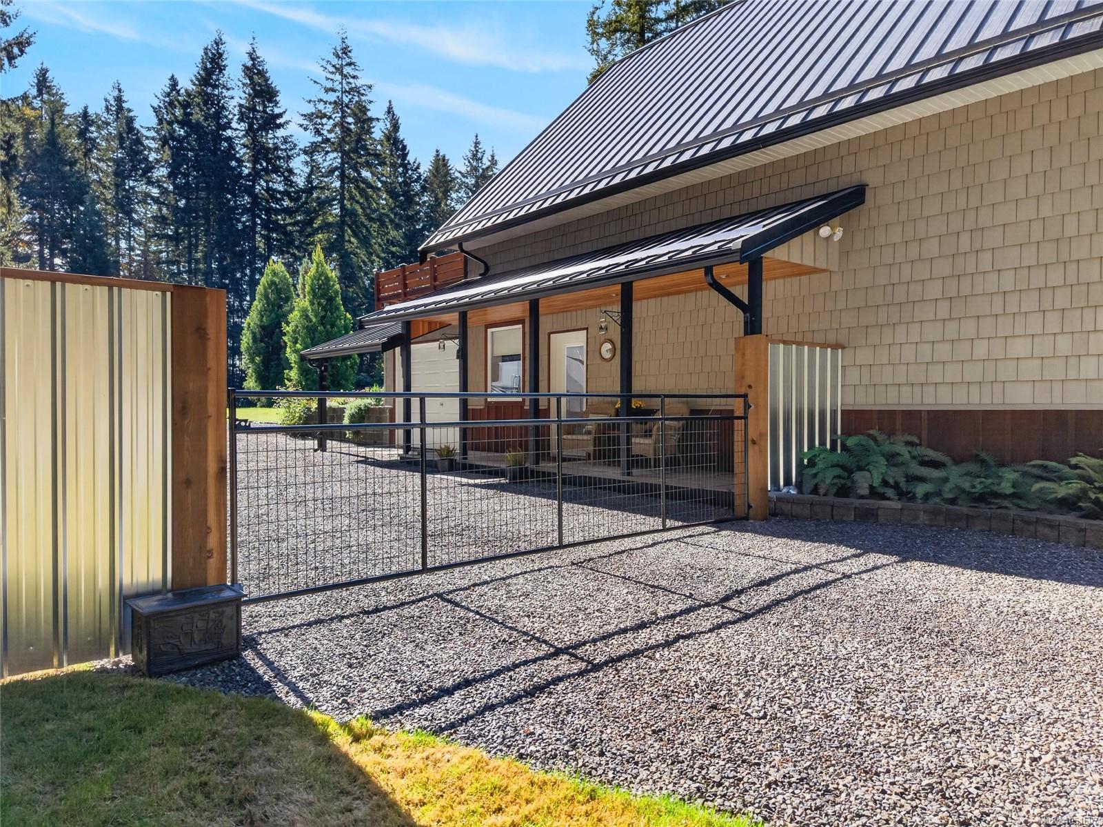 House exterior with a gravel courtyard, metal-and-wood gate, and covered patio entrance.