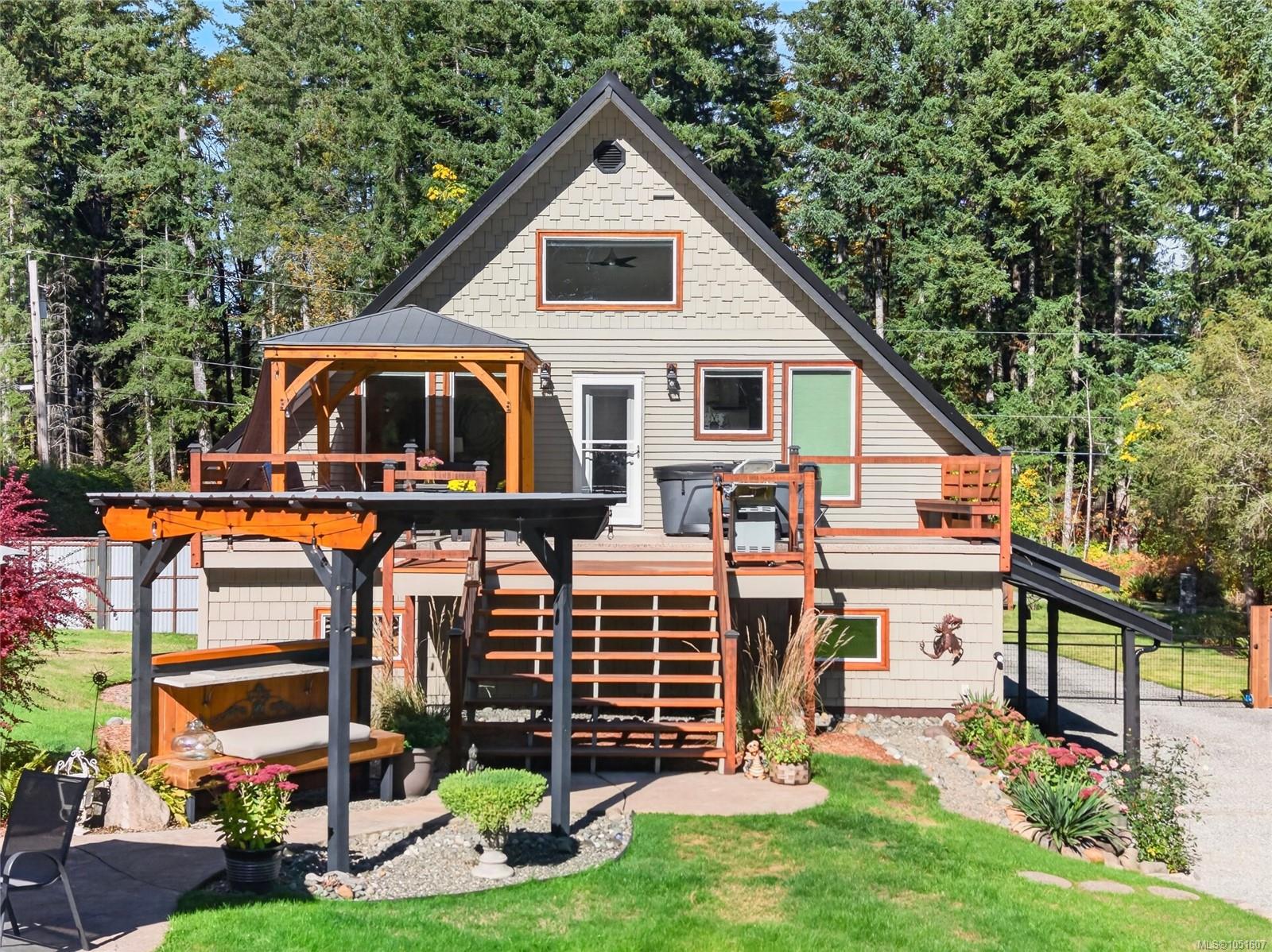 Rear exterior of a home with raised wooden decks, a covered pergola, and landscaped lawn.