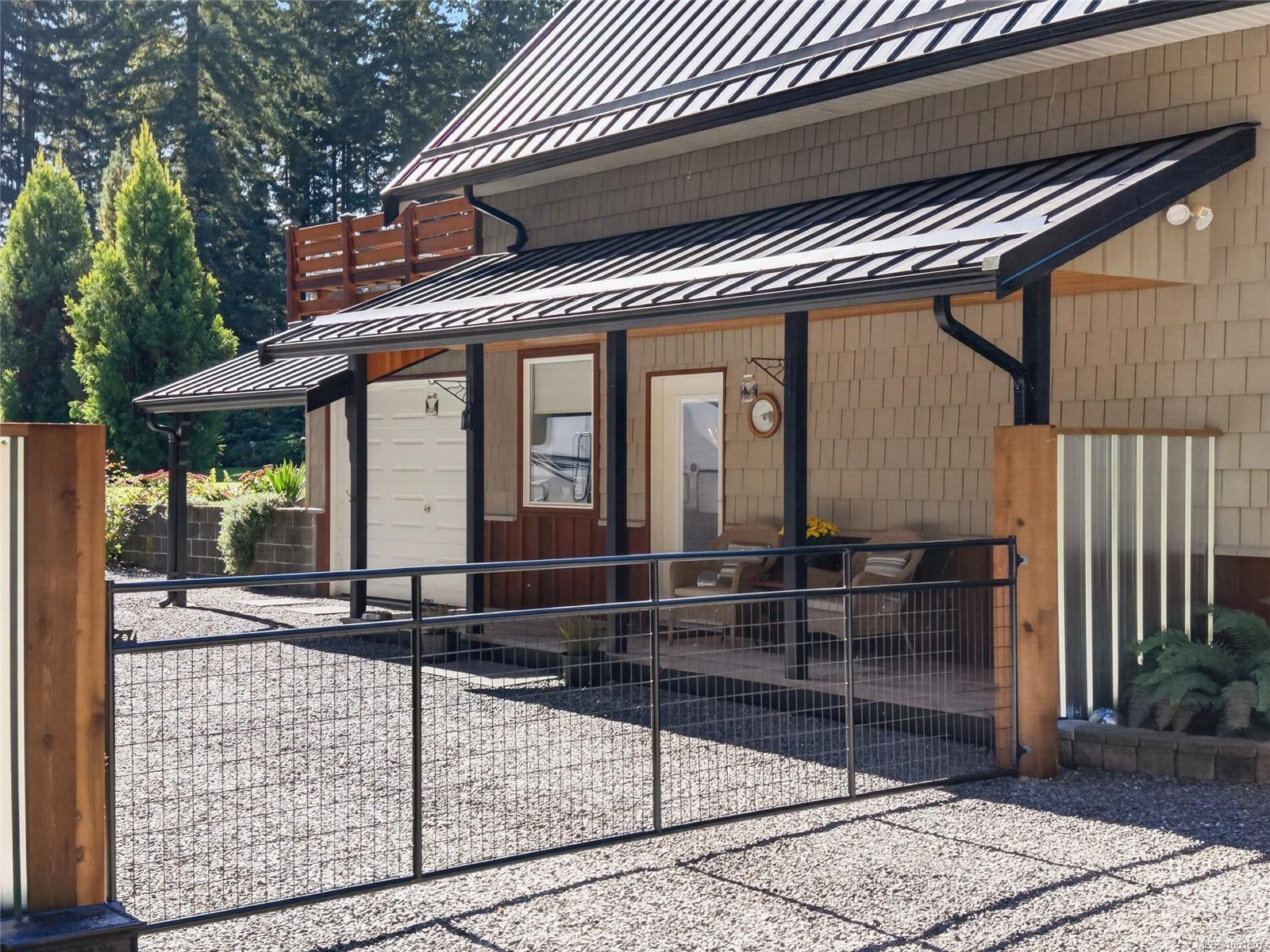 Home exterior with a covered patio and fenced gravel yard beneath metal awnings.