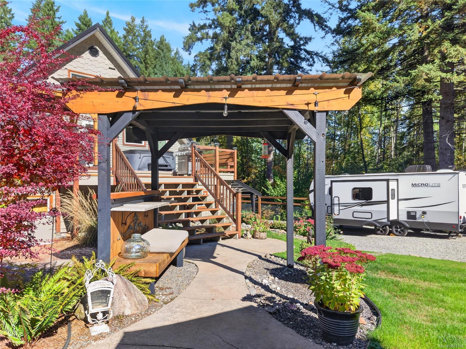 Backyard patio with a timber pergola, raised deck, landscaped garden, and travel trailer.