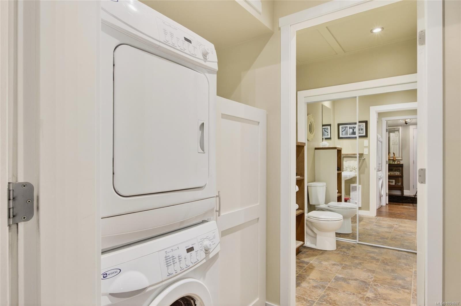 Laundry area with a stacked washer and dryer beside a tiled bathroom with mirrored doors.