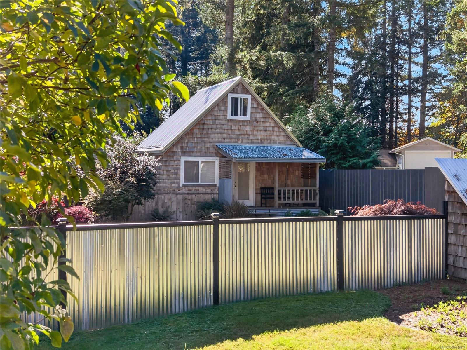 Cedar-shingle house with a steep metal roof and covered porch behind a metal fence.