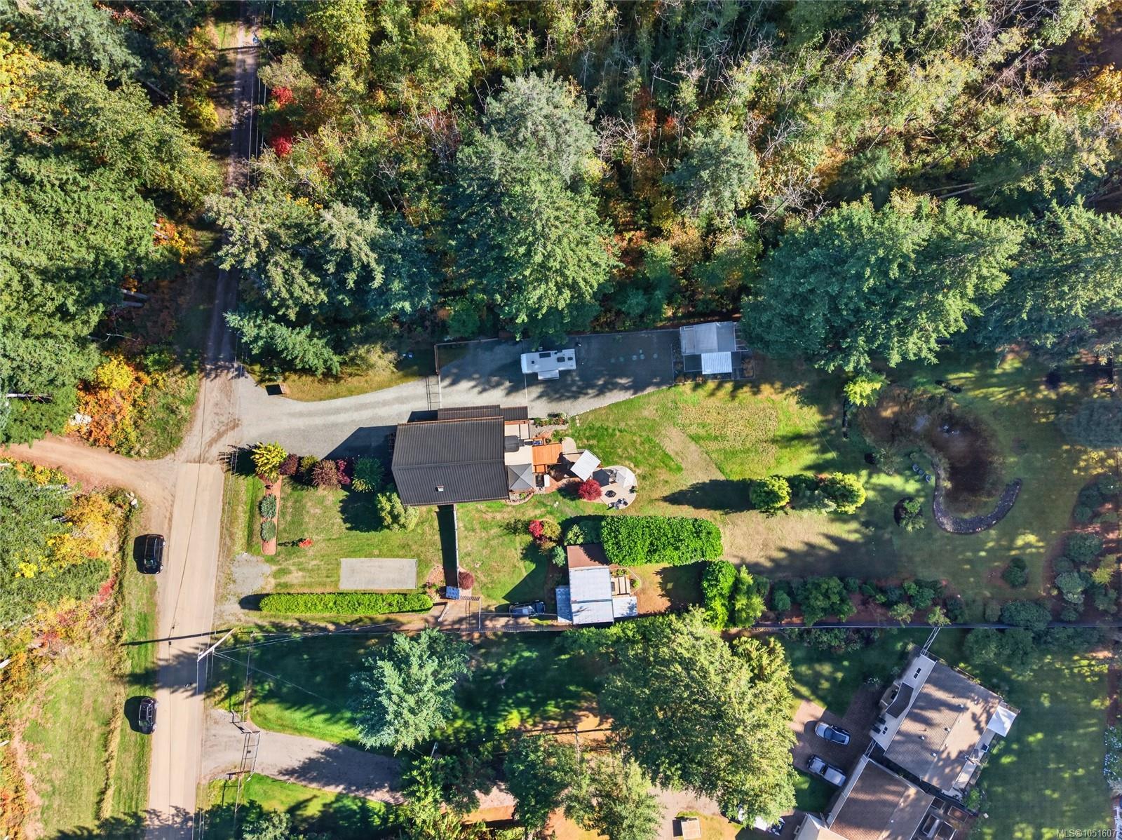 Aerial view of a wooded property with a house, landscaped yard, and gravel driveway.