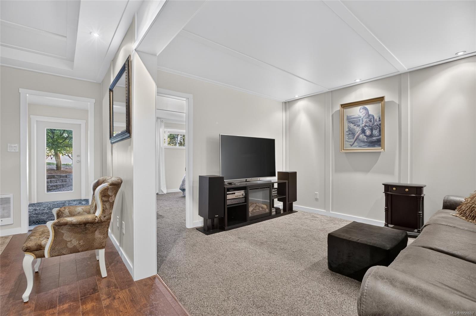 Living room with a television and media console, gray sectional sofa, and tiled entryway.