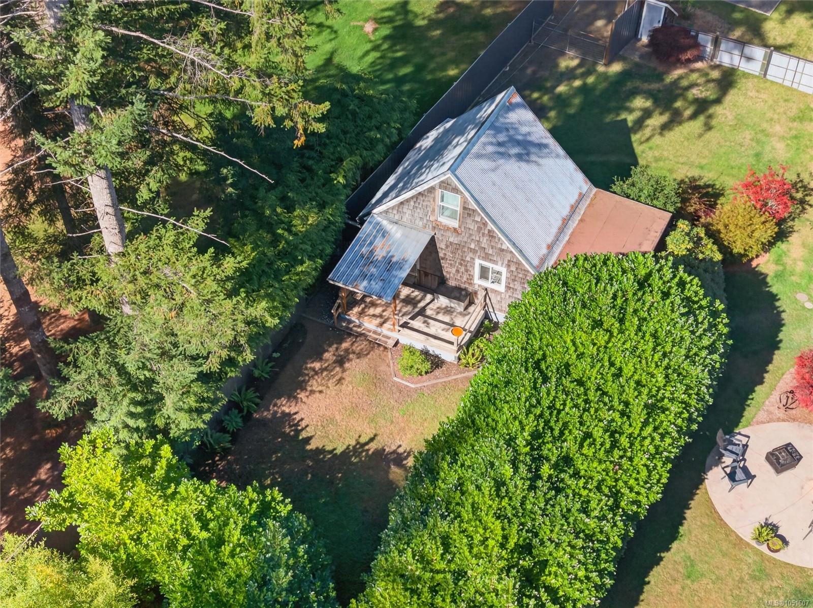 Aerial view of a shingle-sided house with a metal roof, covered porch, and tree-lined lawn.