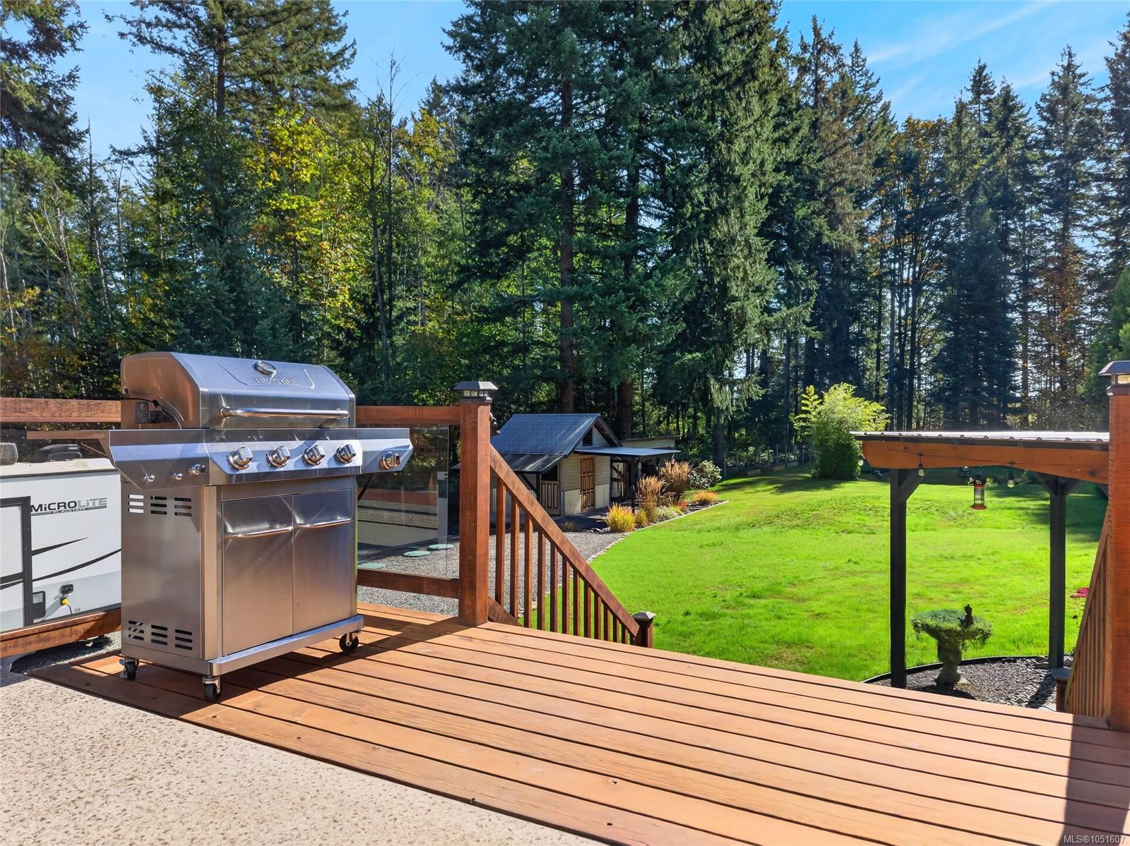 Wooden deck with a stainless-steel grill overlooking a green lawn, garden shed, and wooded backyard.