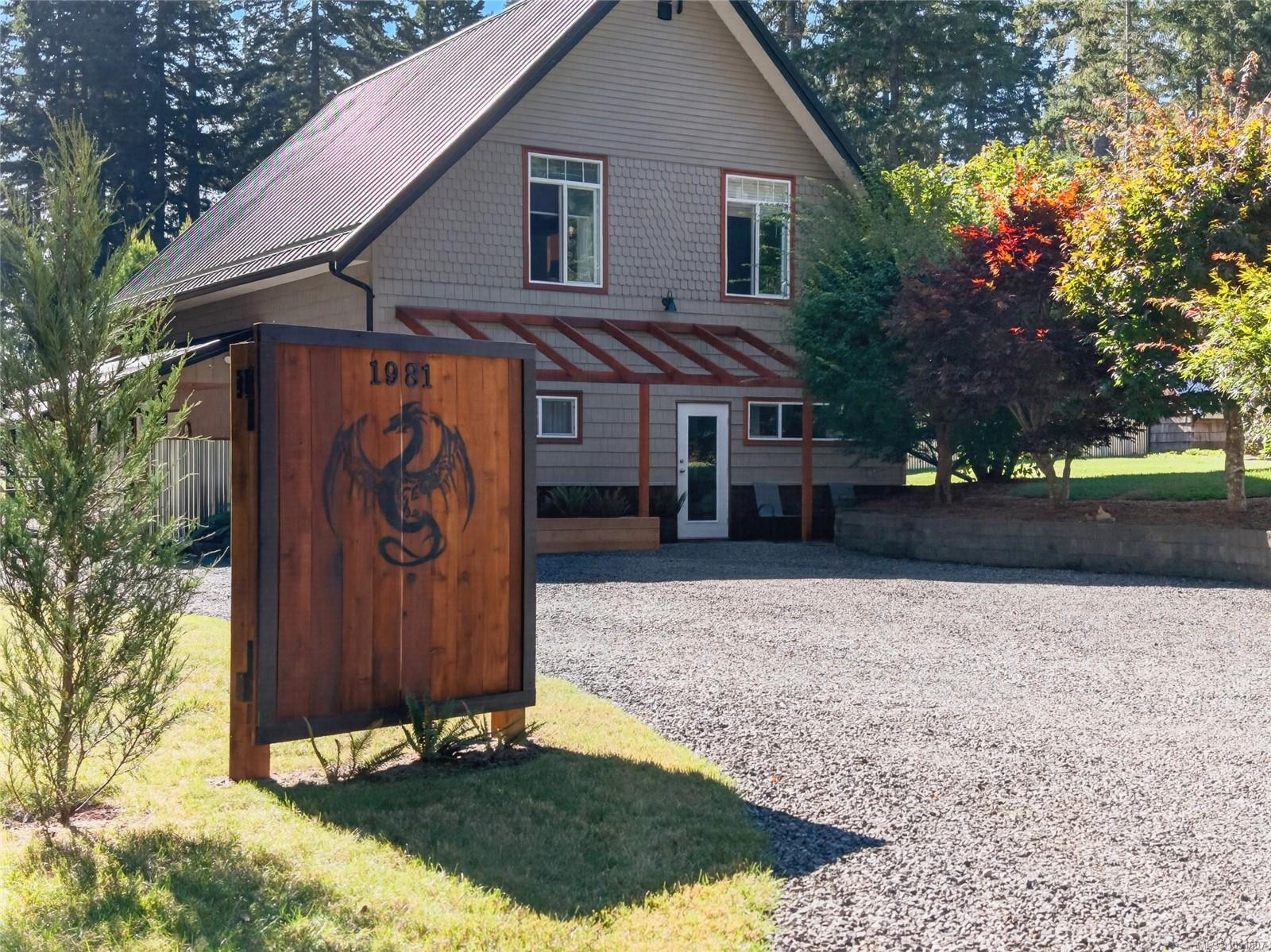 House with a steep metal roof and gravel driveway, behind a wooden sign marked 1981.
