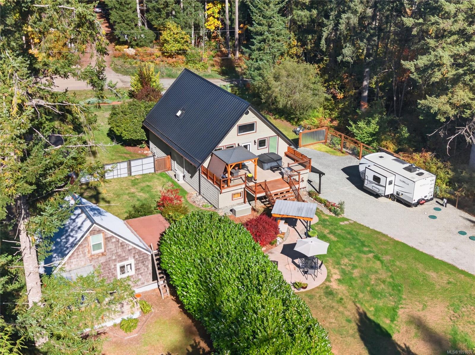 Aerial view of a wooded home with a raised deck, hot tub, and travel trailer.