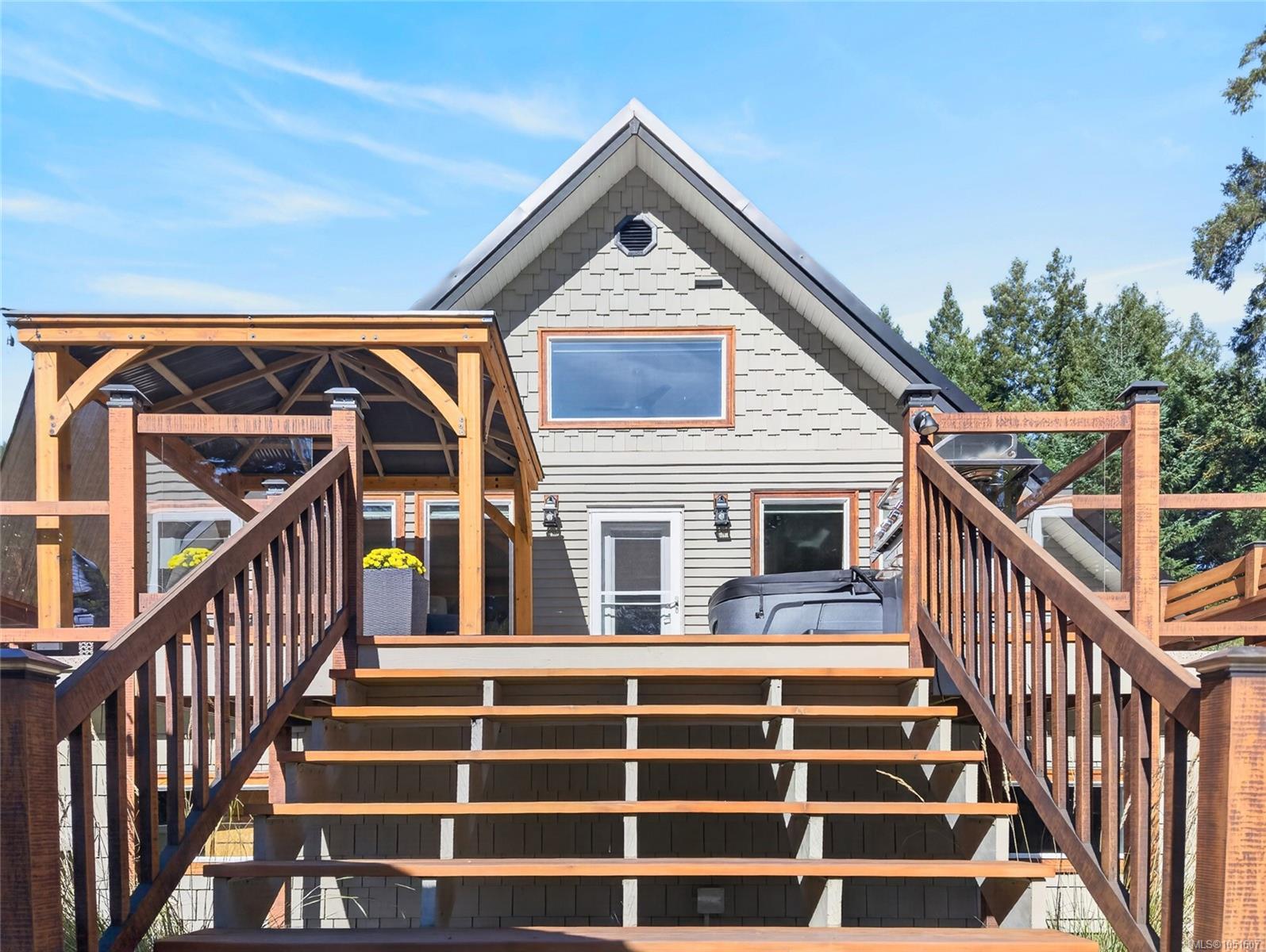 Gray gabled home with broad wooden deck stairs, a timber pergola, and a hot tub.