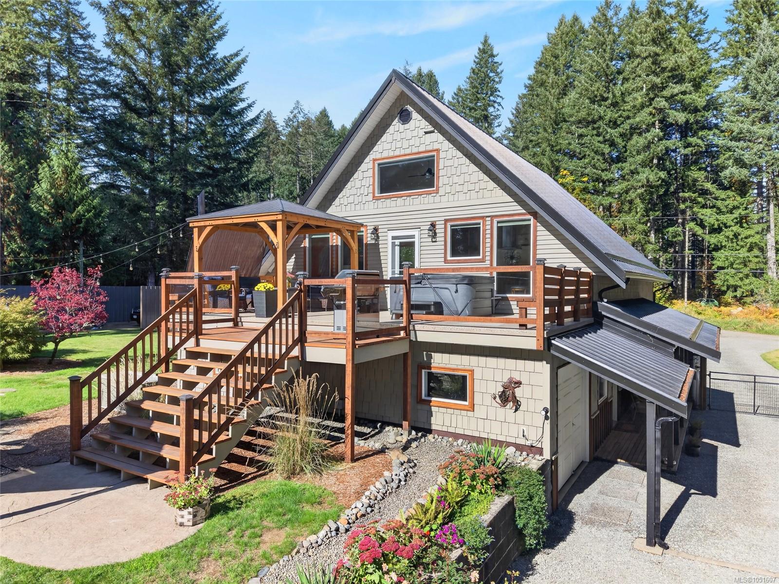 A-frame house with a raised wooden deck, stairs, and hot tub among evergreen trees.