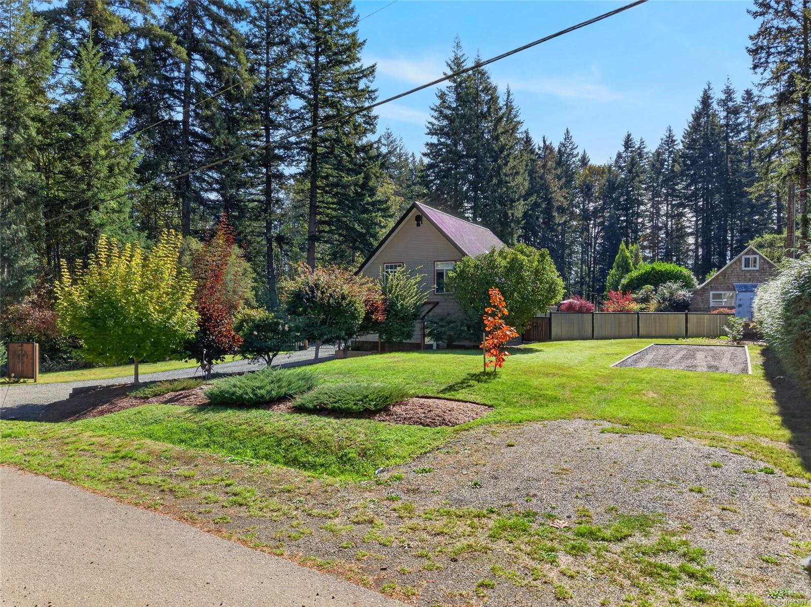 Gabled house with a landscaped lawn, gravel driveway, and evergreen trees.